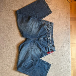 Blå baggy jeans från DNGRS - Säljer ett par blå baggy jeans från DNGRS i storlek 38/34. De har breda ben, snygga broderade detaljer på bakfickorna och har en cool streetstil som passar perfekt till sneakers. Rakt över benöppningen 27 cm, rakt över midjan 48cm, hela benet rakt över 114cm