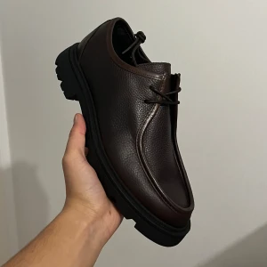 Bianco Biajeff Loafers i Läder - Brown  - Snygga loafers i mörkbrunt skinn med grov, svart platt sula och rund tå. Skorna har snörning framtill och en robust design som passar perfekt till både jeans och chinos. Materialet är präglat skinn som ger en exklusiv känsla.