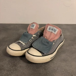 Grå Converse All Star sneakers - Unika Converse All Star sneakers i grått med rosa och blå detaljer på plösen. Låg modell med klassisk vit gummisula och rund tå. Skorna har snörning och är tillverkade i slitstark bomull. Perfekt för dig som gillar en cool och personlig stil.