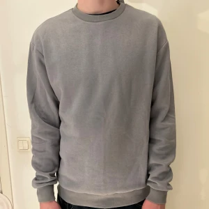 Grå sweatshirt från Jack & Jones - En stilren grå sweatshirt från Jack & Jones med rund hals och ribbade muddar vid ärmslut och nederkant. Tröjan har en enkel design utan mönster och är tillverkad i mjuk bomull, perfekt för chill dagar. Passformen är normal och den har långa ärmar.