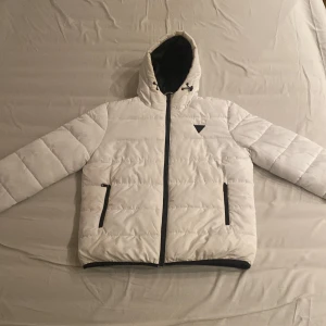 🔥 Vit pufferjacka från guess – Strl L (passar samt strl M också!)  🔥 - Snygg vit pufferjacka från Guess med svart dragkedja, huva och två fickor framtill. Jackan har ett svart Guess-logomärke på bröstet och är fodrad med svart insida. Perfekt för kalla dagar och riktigt clean look.
