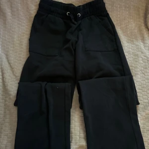 Svarta och vita mjukisbyxor med snörning - Två par mjukisbyxor, ett par svarta och ett par vita, med bred resår i midjan och snörning framtill. Båda har stora fickor fram och bak, raka ben och är tillverkade i mjukt bomullsmaterial. Perfekta för chill dagar eller när du vill vara extra bekväm.