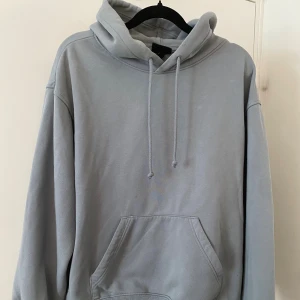 Ljusgrå hoodie med huva och ficka - Enkel och stilren ljusgrå hoodie med huva och dragsko. Tröjan har en stor magficka framtill och långa ärmar. Perfekt för en chill och avslappnad look.