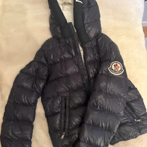 Mörkblå Moncler dunjacka med huva - Säljer en mörkblå dunjacka från Moncler. Kommer ej till användning då den är lite liten. Jättesnygg och trendig vinterjacka!!Modellen är 165, jackan passar som en xs/s💗💗PRIS KAN DISKUTERAS