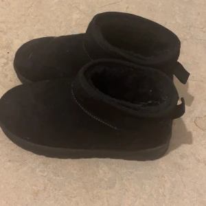 Svarta boots i mocka med pälsfoder - Mysiga svarta boots med rund tå och platt sula, tillverkade i mjuk mocka och fodrade med päls för extra värme. Perfekta för kalla dagar och har en enkel, stilren design med låg skaft och dragflik bak.