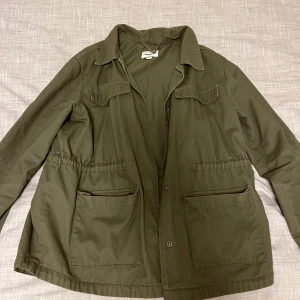 Grön parkajacka från Kappani - Snygg grön parkajacka från Kappani med klassisk krage, stora fickor framtill och knappar. Jackan har en loose passform och är perfekt för dig som gillar en chill och avslappnad stil. Materialet är bomull och jackan har långa ärmar.