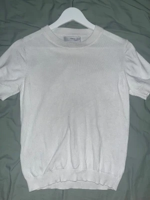Vit stickad kortärmad tröja från MNG - Vit stickad tröja från MNG i storlek S. Tröjan har rund halsringning, korta ärmar och ribbade muddar vid hals, ärmslut och nederkant. Enkel och clean design som funkar till många olika stilar. Perfekt för dig som gillar minimalistiskt och fräscht.