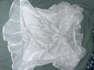 Vit volangklänning från Nelly - Supersöt vit kortklänning från Nelly med flera lager volanger och transparenta detaljer. Klänningen har en romantisk look med rund halsringning och är tillverkad i ett lätt, skir syntetmaterial som ger en fluffig känsla. Perfekt för dig som gillar statement-plagg!