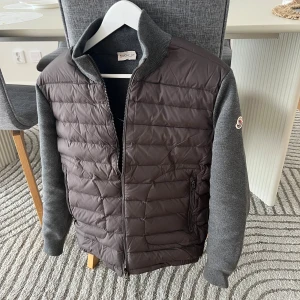Moncler Cardigan  - Snygg Cardigan från Moncler i mörkgrått med stickade ärmar och krage. Jackan har dragkedja framtill, Moncler-logga på ärmen och två sidofickor med zip. Perfekt för dig som vill ha en stilren och modern look. Stl M men passar som S. 