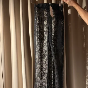 Spetsbyxor från NA-KD XS - Säljer ett par spetsbyxor från NA-KD i storlek XS, helt nya. Byxorna har blommigt spetsmönster i svart färg. Super snygga utsvängda spetsbyxor. Tyvärr passade dem inte mig! 