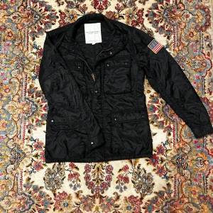 Svart field jacket från Ralph lauren - Snygg svart jacka med amerikansk flagga på ärmen. Flera fickor, dragkedja + knappar. Perfekt för vår/höst. Skriv gärna vid funderingar och frågor