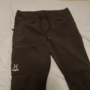 Haglöfs vindbyxor  - Svarta softshellbyxor från Haglöfs i storlek 46. Byxorna har dragsko i midjan, fickor med dragkedja och en stilren logga på benet. Perfekta för utomhusaktiviteter och har en sportig, rak passform. Riktigt bekväma också! Storlek S/M. !!KVITTO FINNS!!
