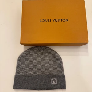 Grå mössa i ull - Exklusiv grå mössa  med diskret rutigt mönster och vikt kant. Mössan är stilren och är tillverkad i mjuk ull, perfekt för kyliga dagar. Snygg accessoar som lyfter din vinterstil.