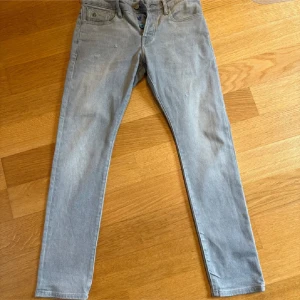Gråa Scotch & Soda Ralston jeans w28 l30 - Snygga grå jeans från Scotch & Soda, modell Ralston. Byxorna har raka ben, klassisk femficksdesign och coola färgade knappar i gylfen. Tillverkade i mjukt bomullsjeansmaterial med diskreta slitningar för en avslappnad look.