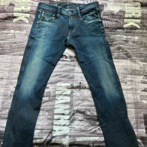 Blå Replay jeans, midwaist, storlek 30/30 - Snygga blå jeans från Replay med klassisk femficksdesign och diskreta slitningar framtill. Jeansen har raka ben och normal passform, midwaist och tydliga kontrastsömmar. Perfekta för dig som gillar en stilren och tidlös look.