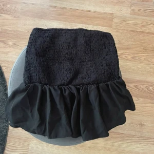 Svart Tubtopp - Säljer en svart tubtopp med volang nedtill. Dem har en cool och ungdomlig vibe, perfekt att styla med sneakers eller boots. Materialet känns lätt och bekvämt, och volangen ger extra rörelse och attityd.