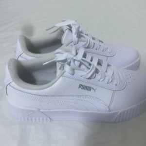 Vita sneakers från Puma Softfoam - Fräscha vita sneakers från Puma med Softfoam-innersula för extra komfort. Skorna har klassisk snörning, rund tå och är tillverkade i syntetmaterial med diskret Puma-logga på sidan. Perfekta för dig som gillar stilrena och sportiga skor.