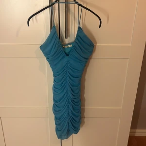 Blå ruched kortklänning NLY One - Supersnygg blå kortklänning från NLY One med tunna axelband och ruched tyg framtill och baktill. Klänningen har v-ringning och är figurnära med en tight passform. Perfekt för dig som vill sticka ut med en fräsch och trendig look.