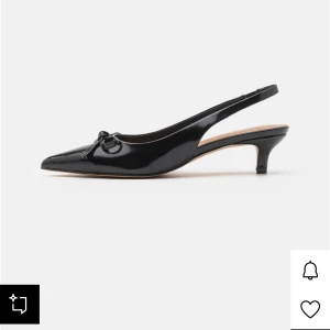 Svarta spetsklackar - Intressekoll på mina snygga svarta pumps från Anna Field med spetsig tå, låg klack och öppen häl. Skorna har en elegant rosettdetalj framtill och är tillverkade i glansigt syntetmaterial. Perfekta för dig som vill ha en stilren och trendig look.