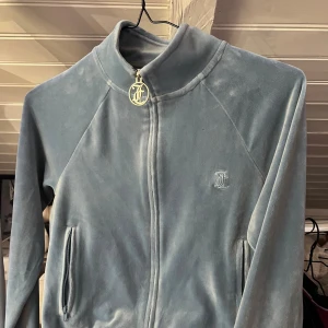 Blå velourkofta från Juicy Couture XS - Supermjuk ljusblå velourkofta från Juicy Couture med glittrande Juicy-text i strass på ryggen. Dragkedja framtill med snygg JC-logga i metall och två fickor. Perfekt för dig som vill ha den ikoniska 2000-talslooken. Säljer pga att jag typ aldrig använt den 🩷