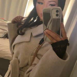 Beige kappa med bälte och  krage - Säljer en snygg beige kappa med bälte i midjan och  krage. Kappan är perfekt för dig som gillar stilrena och trendiga plagg. Materialet känns mjukt och ger en lyxig känsla. Perfekt att slänga på sig över vilken outfit som helst. Pris kan diskuteras!