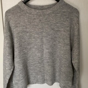 Grå stickad tröja från 157 - Mysig grå stickad tröja från 157 i storlek M. Tröjan har en klassisk rund halsringning och är långärmad. Perfekt för lager-på-lager och enkel att matcha med olika outfits. Materialet är mjukt och ger en avslappnad vibe.