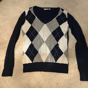 Mörkblå och grå rutig tröja EastWest - Snygg långärmad tröja från EastWest i storlek L med mörkblå, grå och vita rutor i ett klassiskt argylemönster. V-ringad hals och mjukt stickat material som känns skönt mot huden. Perfekt för dig som gillar bekväma men gulliga plagg. Köpt secondhand men säljer då den tyvärr inte är min stil längre. (Gratis frakt om man köper 30 sept-7okt!)