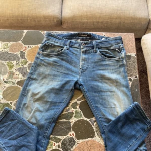 Blå Replay jeans - Säljer ett par blå Replay jeans, modell NUMASIG, med snyggt slitna detaljer och klassisk femficksdesign. Jeansen har raka ben och normal passform, med broderade bakfickor och Replay-logga vid fickan. Perfekta för en avslappnad och cool stil.