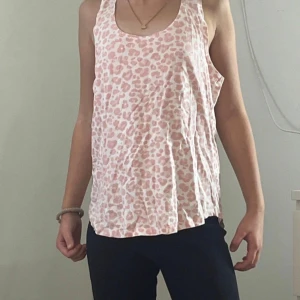 Rosa leopardmönstrad linnetopp - Säljer en ljusrosa linnetopp med leopardmönster i vitt och rosa. Toppen är ärmlös med rund halsringning och har en avslappnad passform. Perfekt för varma dagar och enkel att matcha med jeans eller shorts.