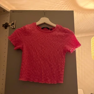 Rosa croppad topp med struktur - Säljer en rosa croppad topp med korta ärmar och smockad struktur. Toppen har en rund halsringning och vågig kant nertill och vid ärmslut. Perfekt för dig som gillar färg och en bekväm, trendig stil.