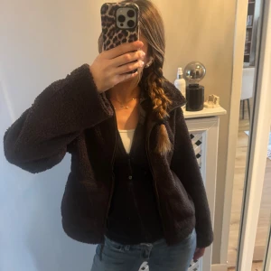Mörkbrun teddyjacka med dragkedja - Den är från H&M och den är slutsåld på webbsidan! Den är lite för kort för mig i magen så kanske till nån annan passar bättre! Jag har haft jackan för två dagar och den är oanvänd! Mysig mörkbrun teddyjacka med hög krage och hel dragkedja framtill. Jackan har en loose passform och är tillverkad i fluffigt fleece-material som håller dig varm. Perfekt för kyliga dagar och enkel att matcha med jeans eller leggings.