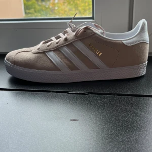 Adidas Gazelle Beige Cream 37 1/3 - Adidas Gazelle J Beige Cream. storlek: 37 1/3 Helt nya och i sin orginalkartong! Lappen på skorna sitter även kvar. Inga defekter helt oanvända. Innersulans längd: 23,5 cm