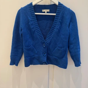 Blå kofta från Essentiel Antwerp - Snygg blå kofta från Essentiel Antwerp. Liten modell. med tre knappar framtill, två små fickor och ribbade detaljer vid ärmslut och nederkant. Koftan har v-ringning och är stickad i ett mjukt material, perfekt för lager-på-lager-stil.