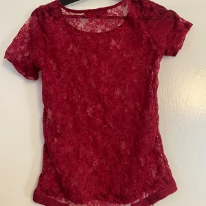 Vinröd spetsblus från ZE-ZE - Säljer en vinröd, transparent spetsblus från ZE-ZE i storlek S. Blusen har korta ärmar, rund halsringning och ett blommigt spetsmönster.