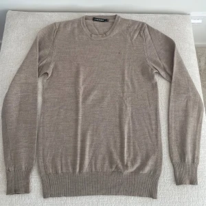 Beige ulltröja från J.Lindeberg - Snygg beige tröja från J.Lindeberg i mjuk ull. Klassisk rund halsringning och långa ärmar med ribbade muddar. Perfekt för lager-på-lager och stilrena outfits.