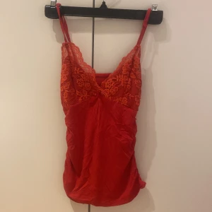 Röd spetslinnetopp från SHEIN - Säljer en röd linnetopp från SHEIN med smala axelband och v-ringad spets upptill. Toppen har en liten rosett framtill och fina blommiga spetsdetaljer. Materialet är mjukt och lätt, perfekt för varma dagar eller lager på lager.