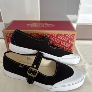 Svarta Vans Mary Jane sneakers - Helt oanvända nya svarta Vans Mary Jane sneakers i canvas med vit gummisula och klassisk brun Vans-undersida. Skorna har rund tå, kontrastsömmar och en justerbar rem med metallspänne över foten. Perfekt för dig som gillar en mix av street och retrostil. Nypris 799:-  !!Finns på fler sidor!!