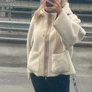 Beige teddyjacka med huva och dragkedja - Mysig beige teddyjacka med huva, stora fickor framtill och dragkedja hela vägen. Den går även att vända ut och in till beige mocka jacka. Nypris 3000 kr, köpt på Sandhamn.