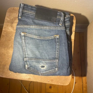 Blå jeans från Massimo Dutti - Snygga blå jeans från Massimo Duttu med klassisk femficksdesign och slitning på bakfickan. Jeansen har en mörk tvätt och tydliga kontrastsömmar. Perfekt för dig som gillar en avslappnad och cool stil. Hål på knät