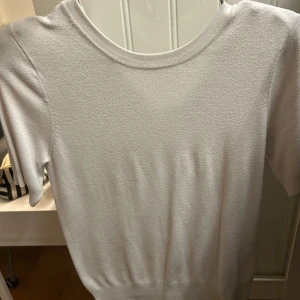 Vit kortärmad tröja från Zara - Säljer en stilren vit kortärmad tröja från Zara med rund hals och tryckknappar vid axeln. Tröjan är i mjukt material och har en enkel, clean look som passar perfekt till jeans eller kjol.