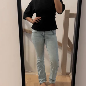Ljusblå raka jeans - Säljer ett par ljusblå jeans med klassisk femficksdesign och raka ben. Jeansen har normal midja och är tillverkade i mjukt denimtyg som ger en avslappnad känsla. Perfekta för dig som gillar en enkel och stilren look.