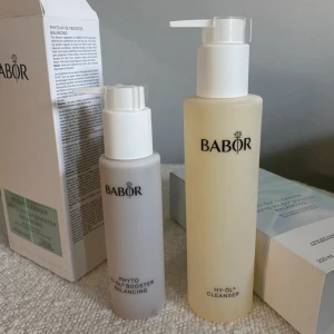 Babor HY-ÖL Cleanser & Booster Balancing - Babor HY-ÖL Cleanser och Phyto HY-ÖL Booster Balancing är ett tvåstegs rengöringskit för kombinerad hud. Setet innehåller en gulaktig rengöringsolja och en vit booster, båda i stilrena plastflaskor med pump. Förpackningarna är eleganta med holografiska detaljer.