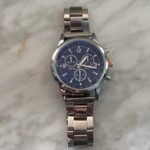 Blå kronografklocka med metallarmband - Stilren klocka med blå urtavla och silverfärgade detaljer. Finns dock en liten spricka vid sidan som gör att den kostar så lite men de tänker man inte på. Klockan har tre mindre urtavlor, tydliga siffror och robust länkarmband i metall. Perfekt accessoar för dig som gillar klassisk och sportig sti