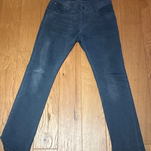 Mörkblå jeans från Nudie Jeans 31/32 - Snygga mörkblå jeans från Nudie Jeans i klassisk straight fit. Jeansen har fem fickor, subtila slitningar och Nudie Jeans signaturbroderi på bakfickorna. Tillverkade i mjukt bomullsmaterial med knappgylf. Perfekt för dig som gillar stilrena och tidlösa jeans. Säljer pågrund av att jag går igenom min garderob just nu!