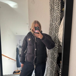 Mörkblå/Lila pufferjacka från CAYA - Säljer en snygg jacka från märket Caya. Köpt förra vintern men knappt använd! Färgen är mörkblå/lila med lite skimmer från solljus (se bild). Jag hittar inte någonstans att köpa den längre. Armarna har en dragkedja vilket betyder att jackan kan bli en väst också!