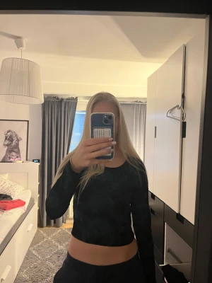 Svart och grön/blå croppad topp från Monki - Säljer en croppad långärmad topp från Monki i svart med grön/blått abstrakt mönster. Toppen har rund halsringning och är figurnära i passformen. Materialet är mjukt och stretchigt, perfekt för dig som gillar coola prints och vill ha en snygg siluett.