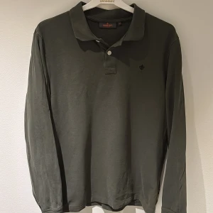 Mörkgrön långärmad pikétröja från Morris - Snygg mörkgrön långärmad pikétröja från Morris med klassisk krage och två knappar framtill. Tröjan har en mörk Morris logga vid bröst. Tröjan är liten i storleken och därmed bättre passande för någon med S. Har av dig vid funderingar