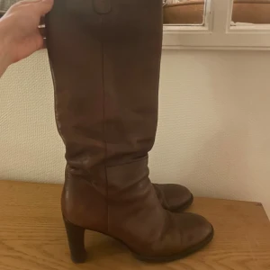 Bruna skinnstövlar med klack  - Säljer ett par snygga bruna stövlar från Rizzo. Stövlarna är i äkta skinn och har en rund tå samt en klack som ger extra höjd. Klassisk design, perfekt för dig som gillar tidlös och elegant look. 