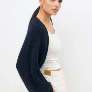 Mörkblå stickad bolero - Säljer en mörkblå stickad bolero. Koftan är enkel och stilren, perfekt att slänga över ett linne eller t-shirt. Mjuk och skön, passar till både jeans och kjol. Den är från Gina men säljs inte längre. Helt oanvänd