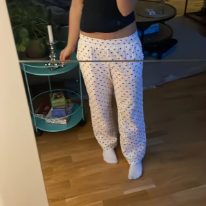 Vita mjukisbyxor med röda hjärtan  - Supermysiga vita mjukisbyxor från X3 med gulligt rött hjärtmönster. Byxorna har elastisk midja och är gjorda i en blandning av återvunnen och ekologisk bomull. Perfekta för chill hemma eller sleepover med kompisarna.